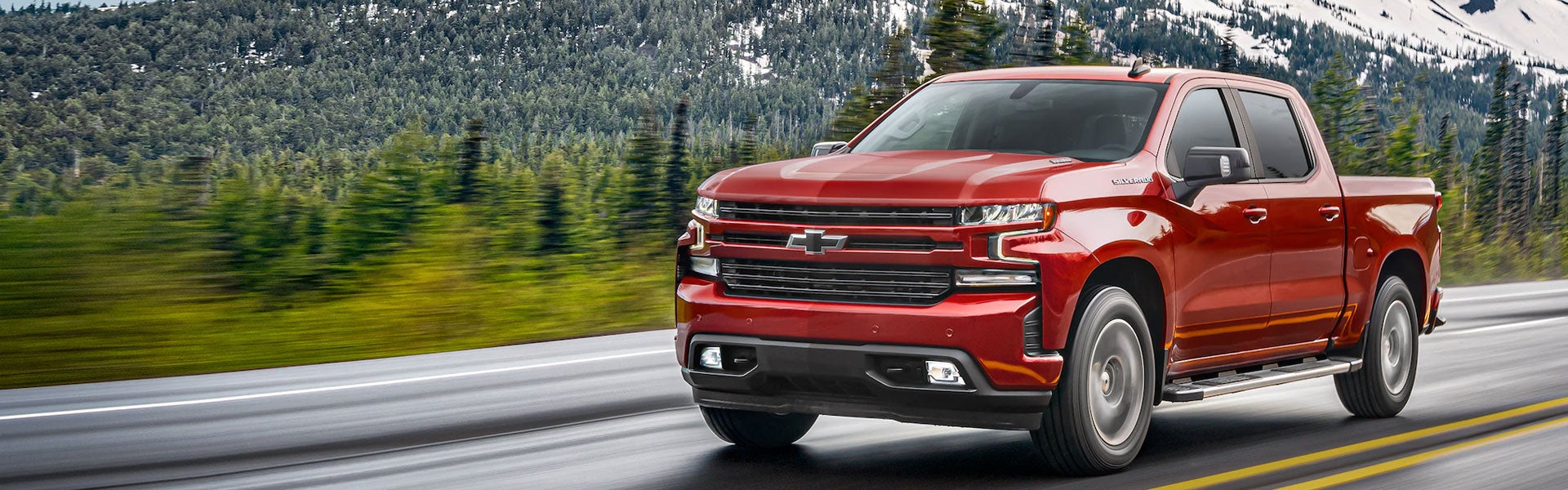 Red 2021 Chevy Silverado driving on road by snow covered mountains