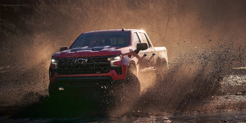 Red Chevy Silverado 1500 driving through muddy puddle in desert